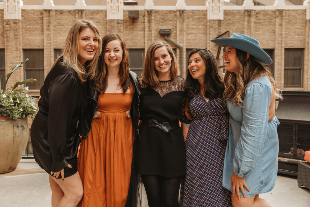 Five women in formal dresses laughing together outside